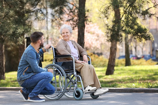 Senior woman in wheelchair with young man at park